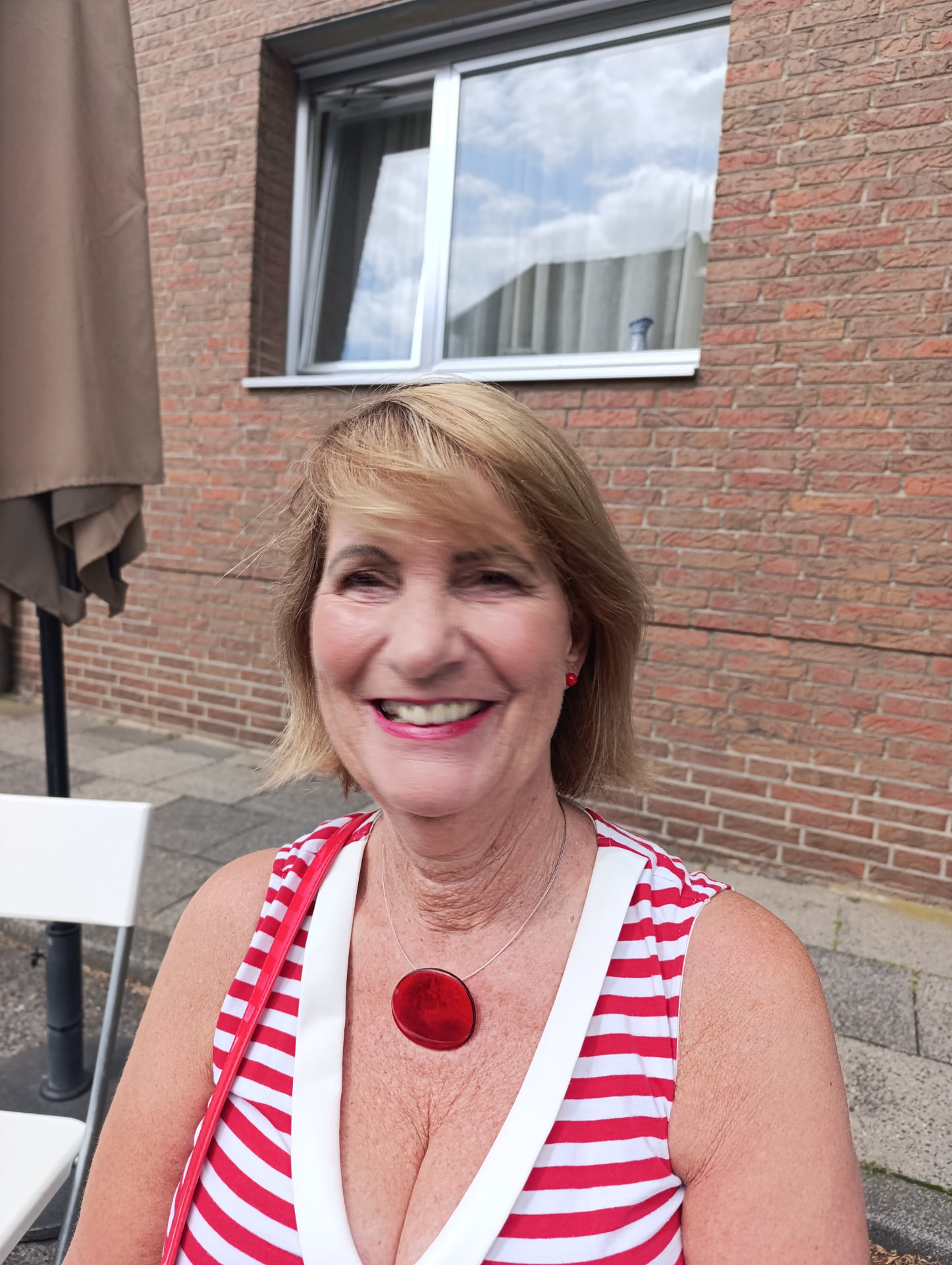 Lächelnde Kundin mit natürlichem Tages-Make-up und rotem Lippenstift vor einer Klinkerfassade