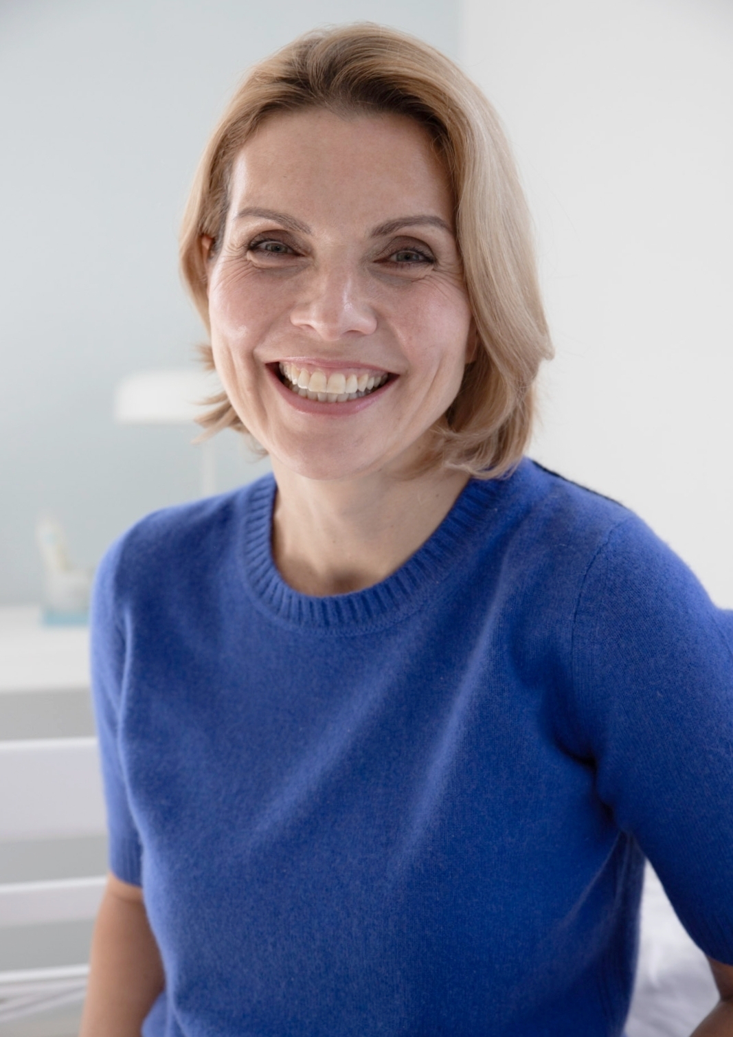 Lächelnde Frau mit frischem Business-Make-up in blauem Pullover vor hellem Hintergrund